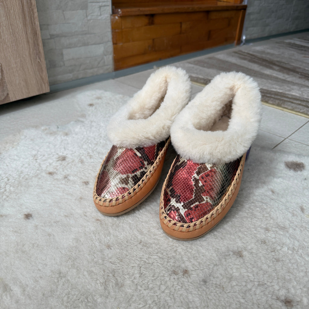 Person wearing patterned slippers with white fur lining on a textured floor.